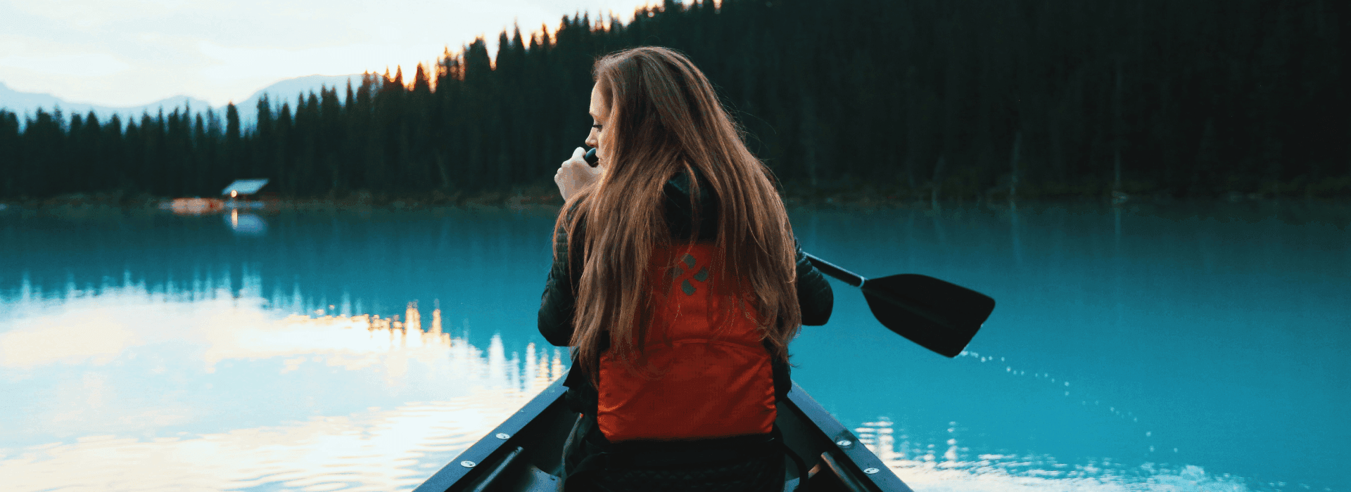 Traveller paddling a canoe on a still lake at sunrise